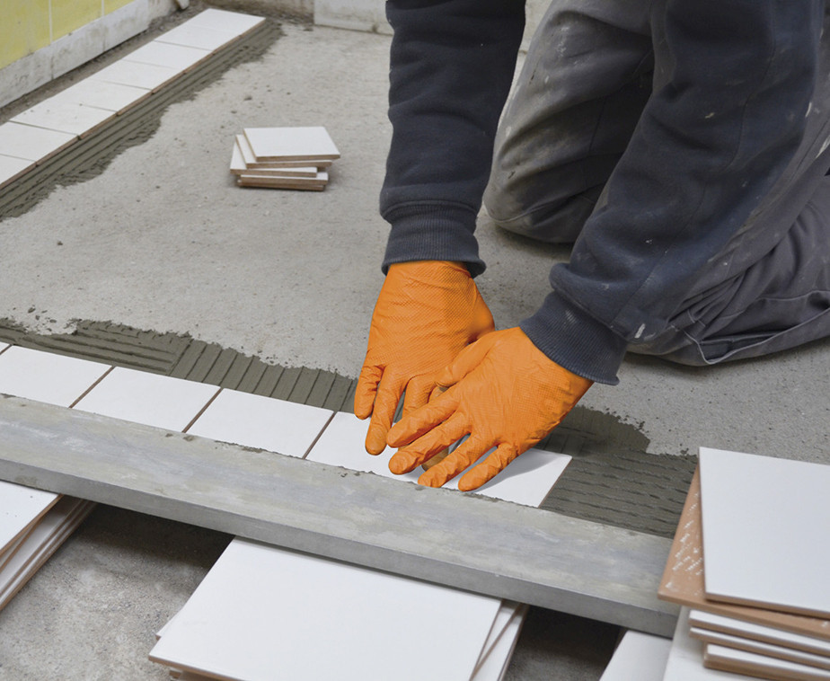 Une personne avec des gants de protection posant du carrelage